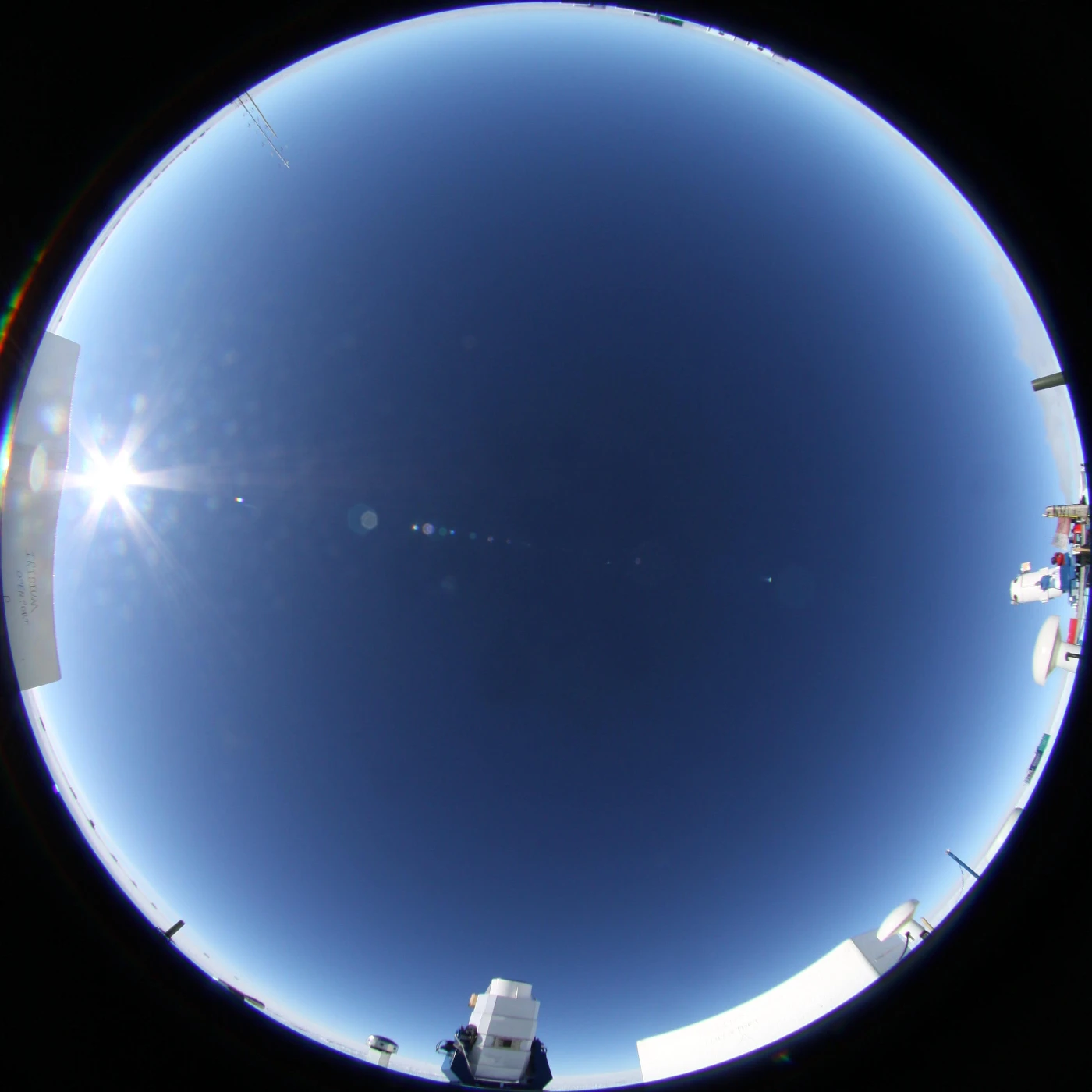 An all sky image of showing the two AST3 telescopes on the upper and right hand side. The bright spot at the bottom shows the Sun.